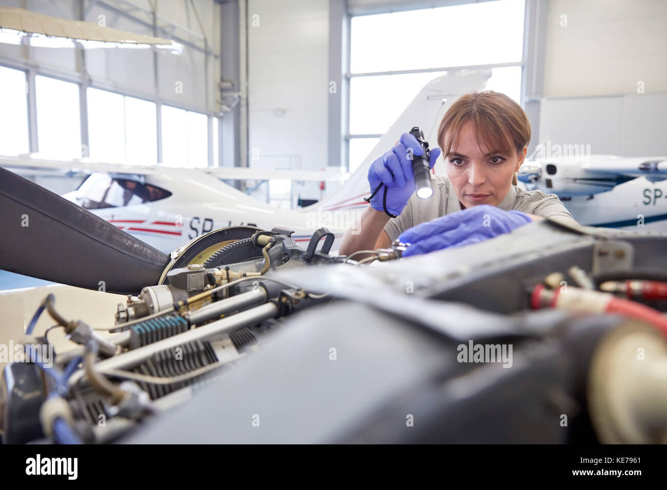 Focused female engineer mechanic with flashlight examining airplane engine in hangar Stock Photo