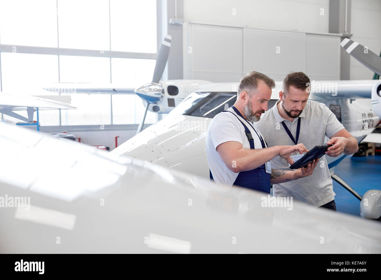 Male mechanic engineers using digital tablet near airplane in hangar Stock Photo