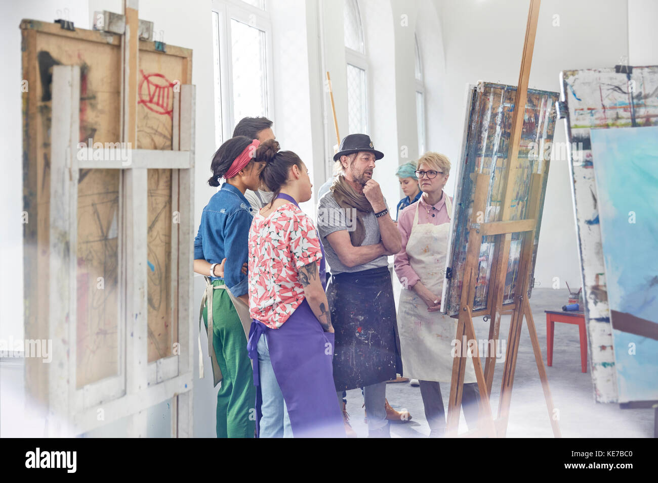 Art students and instructor examining, critiquing painting in art class studio Stock Photo
