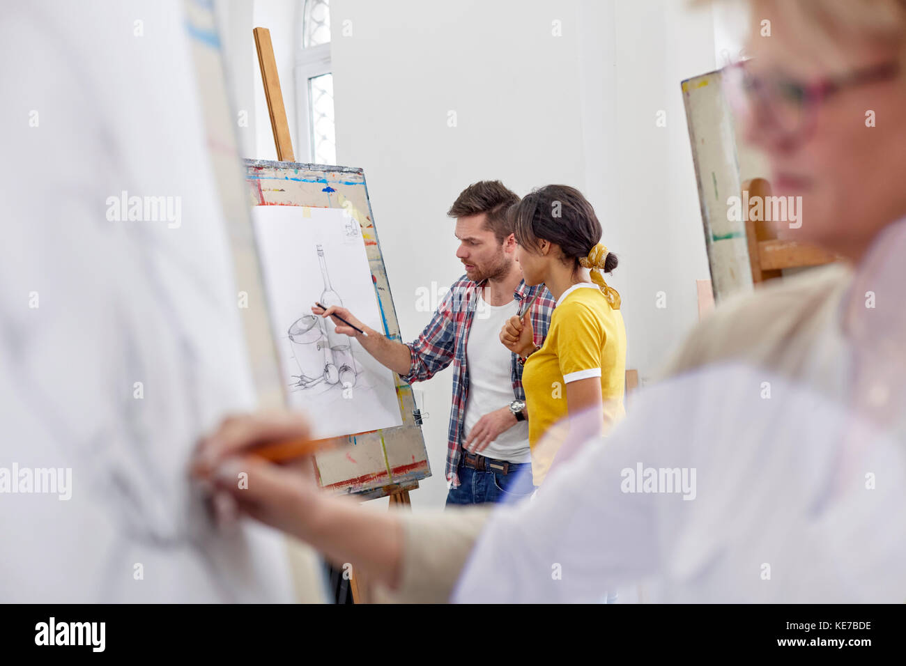 Artists discussing sketch at easel in art class studio Stock Photo