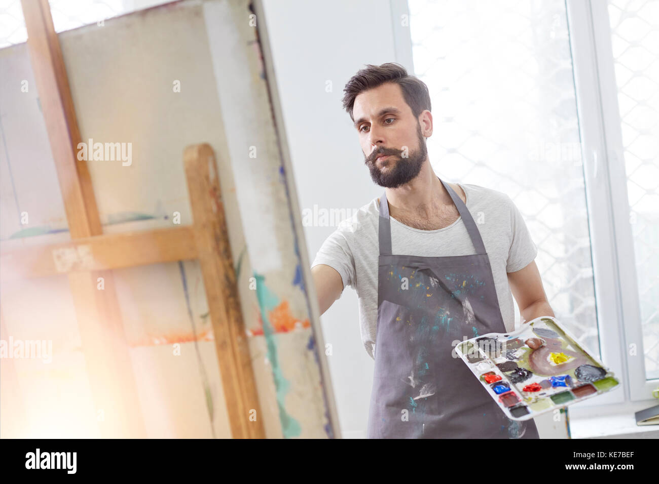 Male artist with palette painting at easel in art studio Stock Photo