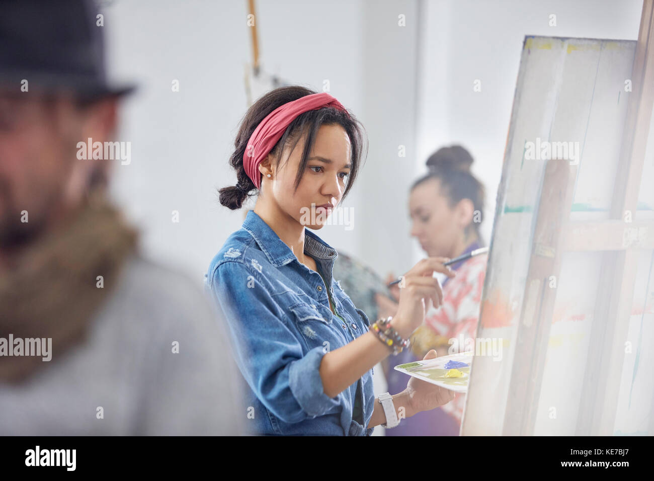 Focused female artist painting at easel in art class studio Stock Photo