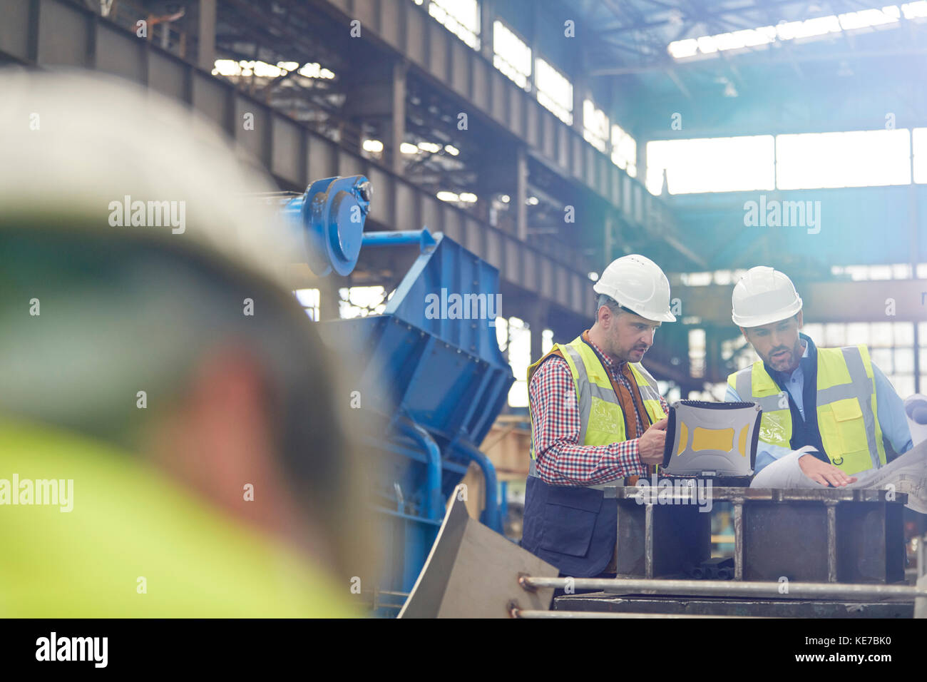 Male foreman and engineer working at laptop, discussing blueprints in factory Stock Photo