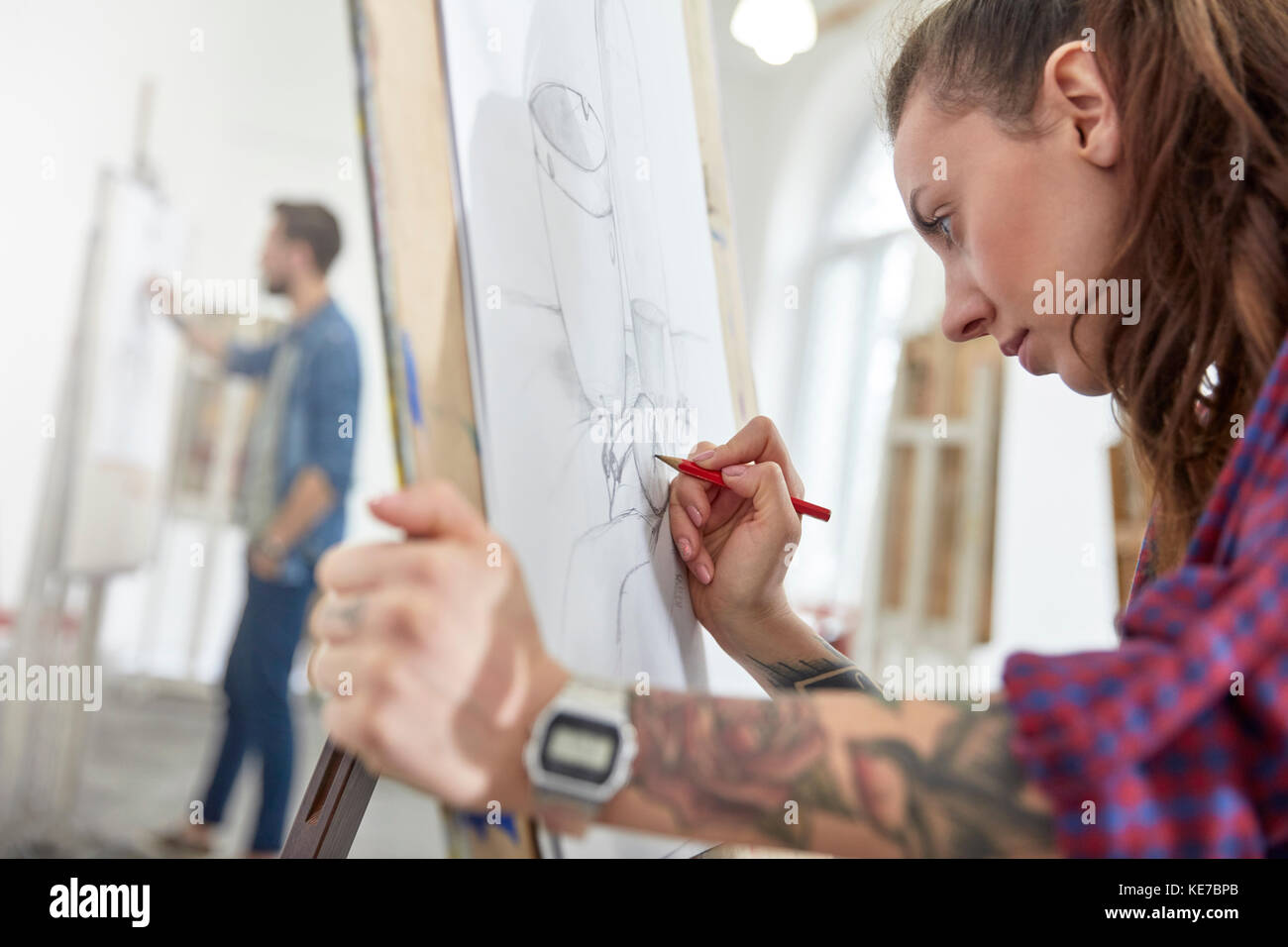 Focused female artist with tattoo sketching at easel in art class studio Stock Photo
