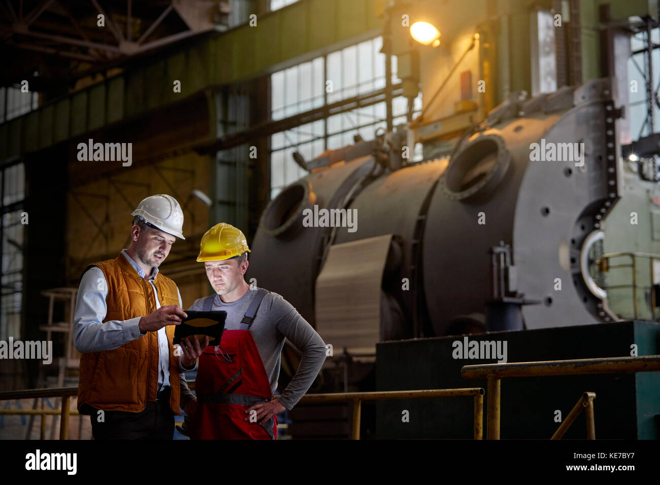 Male engineer and worker using digital tablet in dark factory Stock Photo