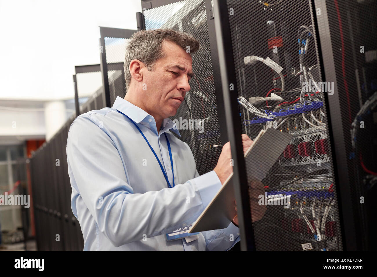 Male IT technician writing on clipboard at panel in server room Stock Photo