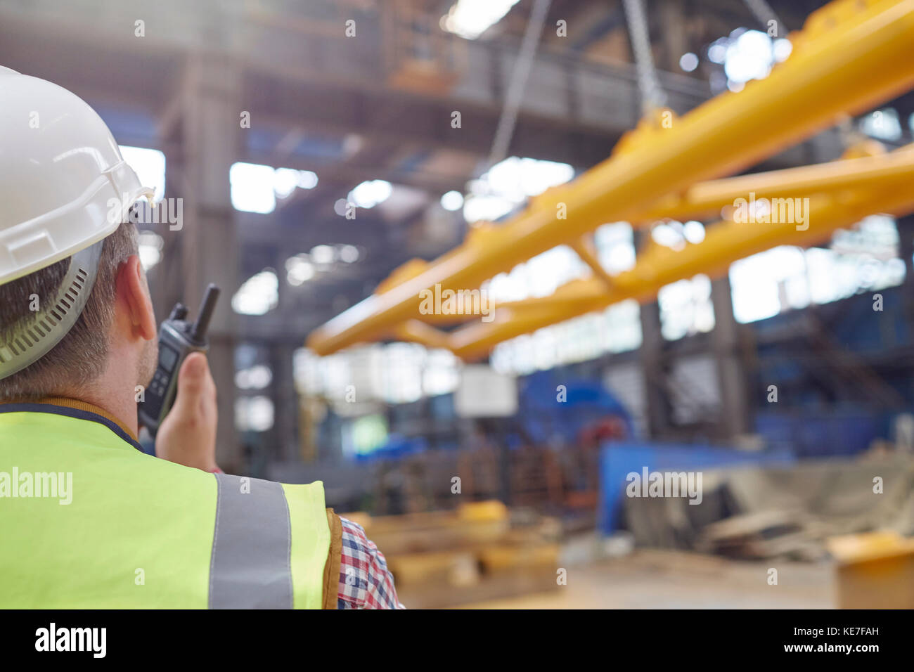 Male worker using walkie-talkie to guide hydraulic crane lowering equipment in factory Stock Photo