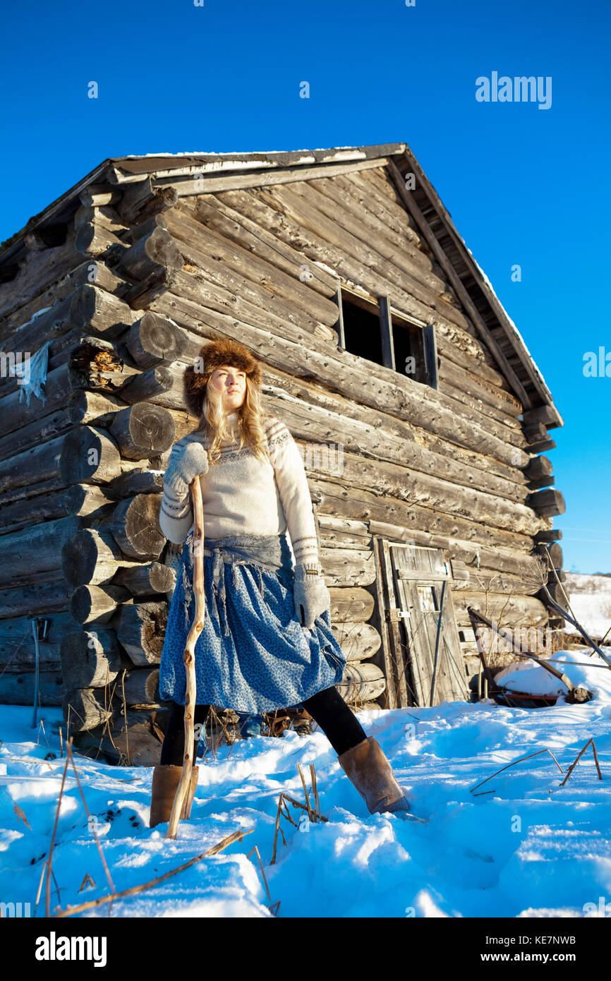 A Girl With A Fur Hat Stands In The Snow With A Walking Stick And