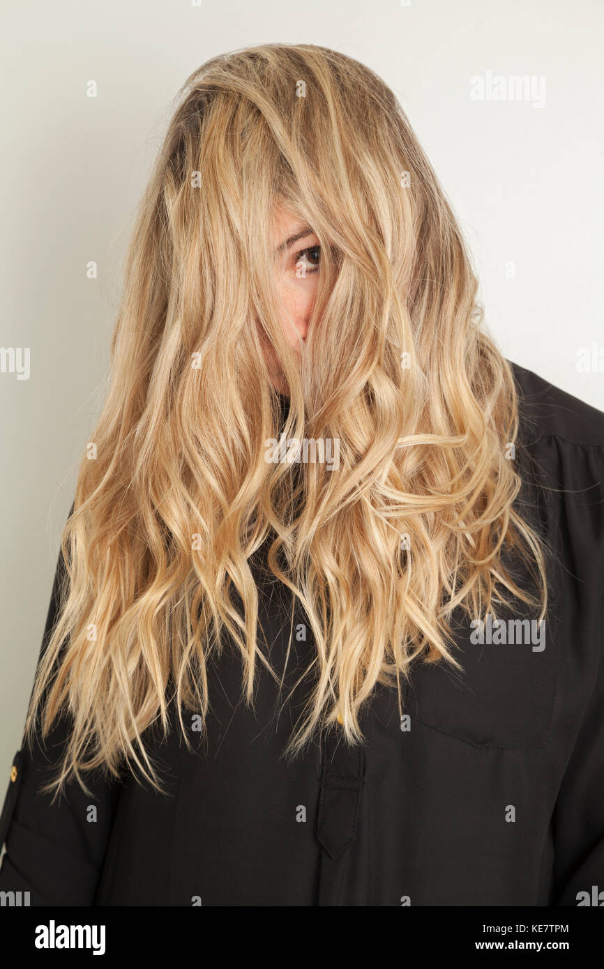 Young Woman With Long Blond Hair Looking At The Camera With One Eye And Her Hair Covering Her Face; Connecticut, United States Of America Stock Photo