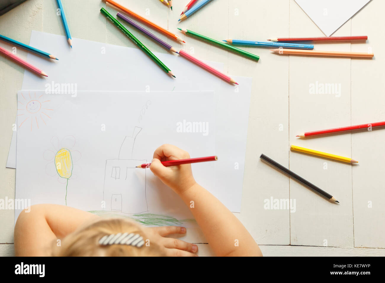 The girl draws her house with colored pencils. Stock Photo