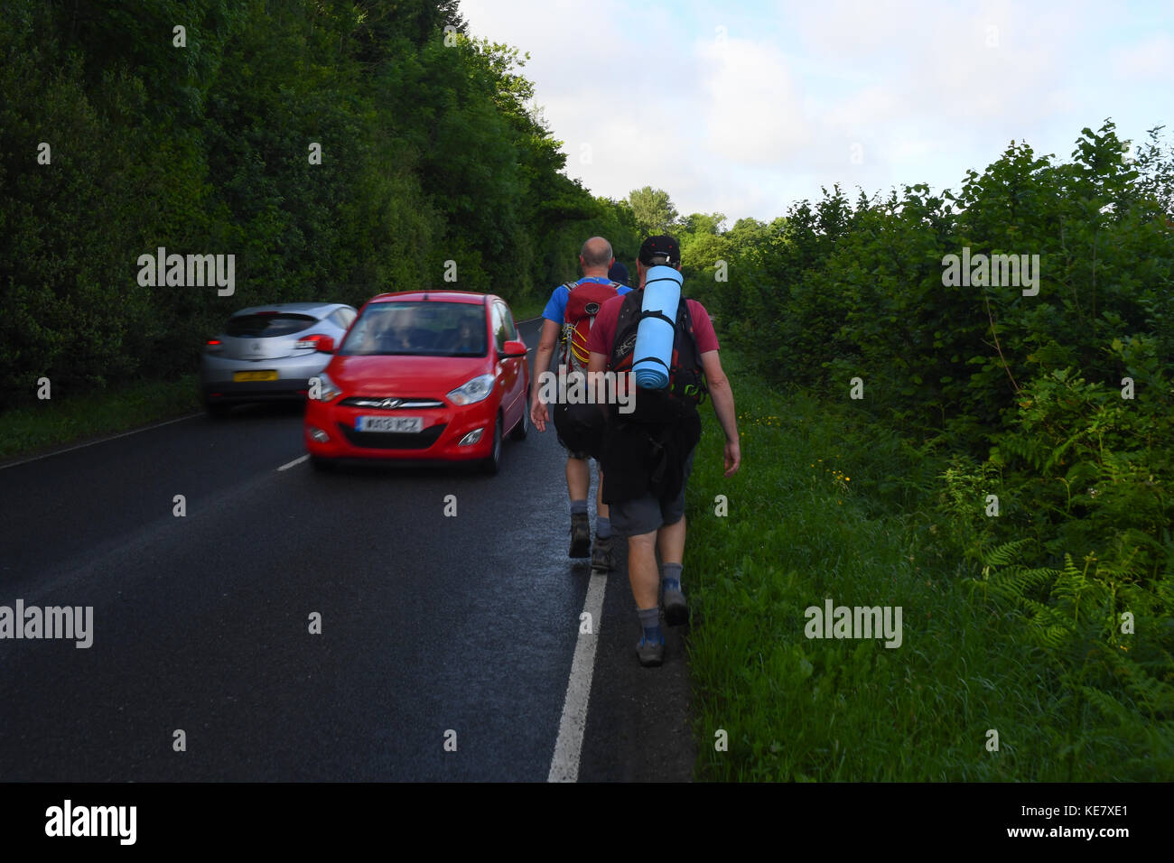 Ramblers walk up a road without a footpath into oncoming traffic Stock Photo