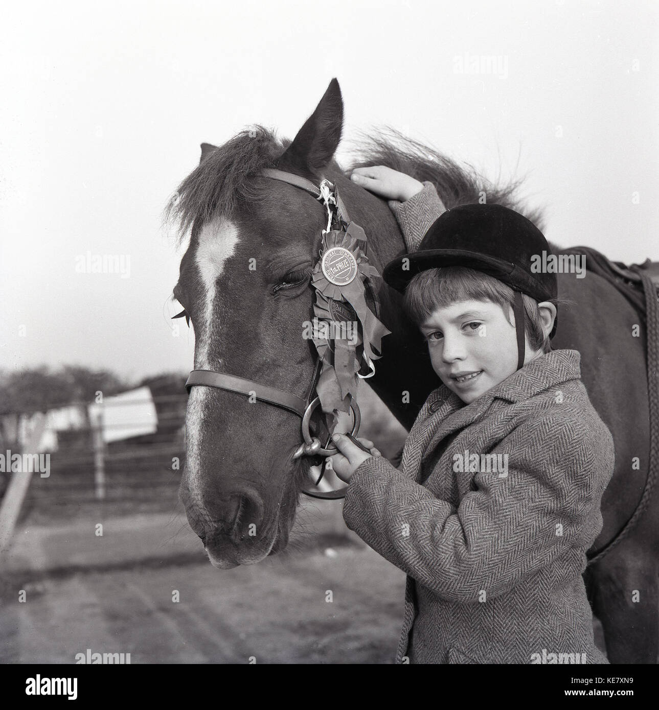 Girls love horses.....in this historical picutre from the 1960s, we see a sweet young girl wearing a riding hat and tweed jacket holding her horse affectionately with one hand and the other hand holding  its bridle, attached to which are prize-winning rosettes, England, UK. Stock Photo