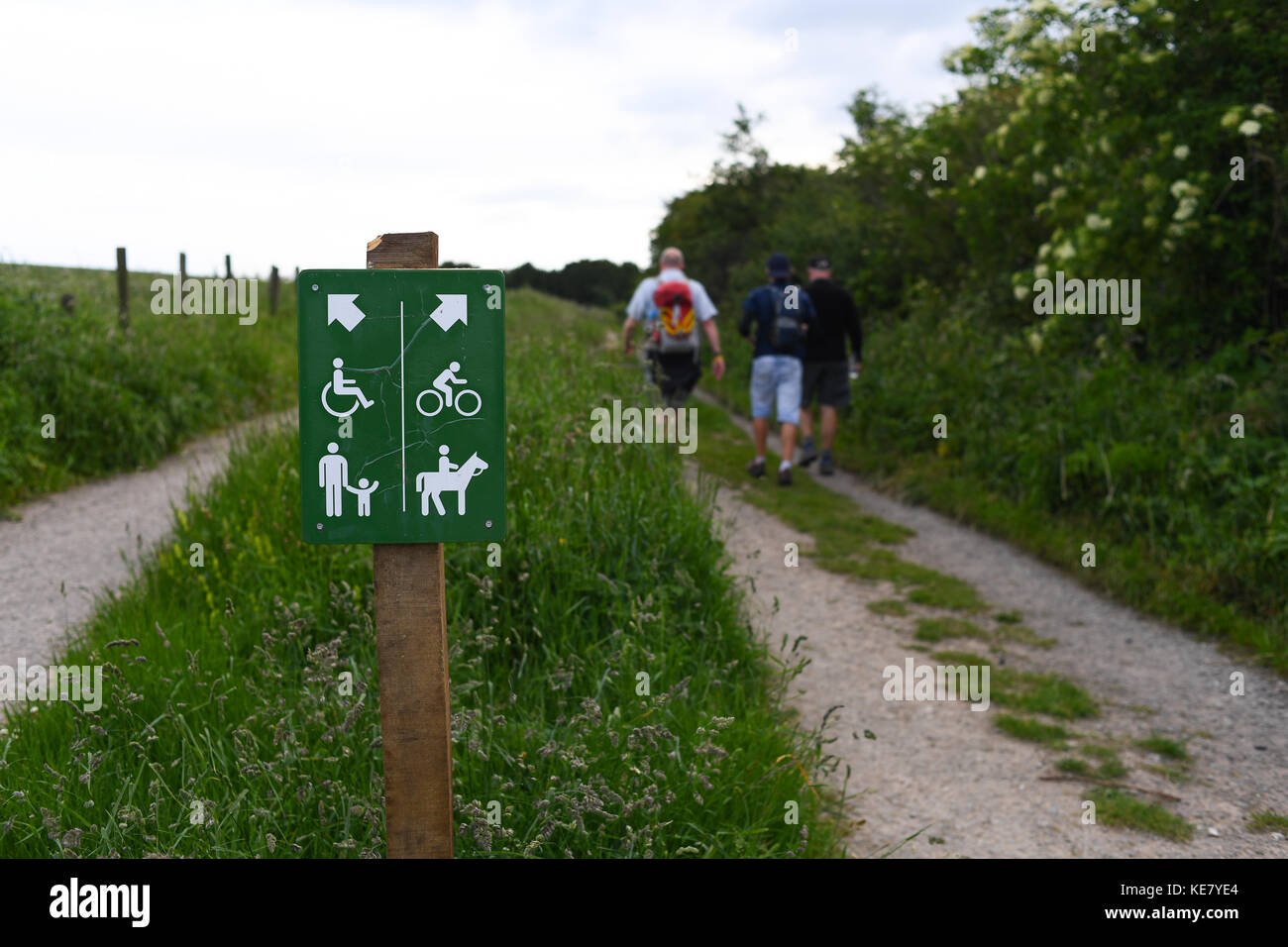 Ramblers walking on the South Downs way from Winchester to Eastbourne next to a  sign showing access rights for paths and trails for multiple users. Stock Photo