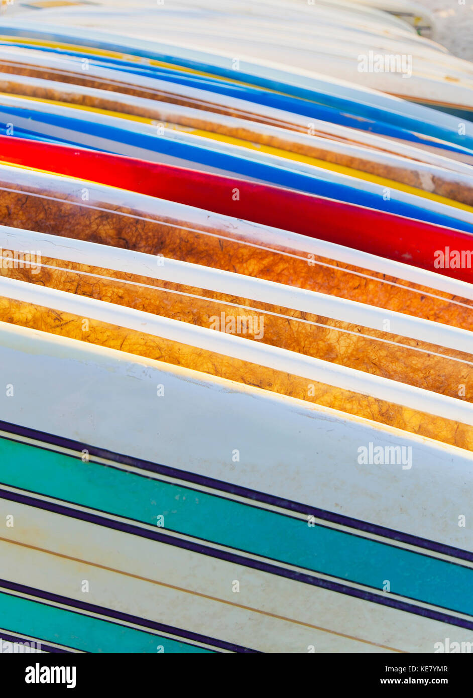A stack of colourful longboard surfboards placed on the beach,; Waikiki
