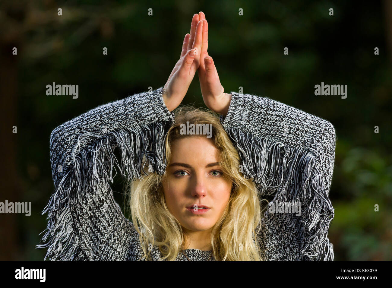 Girl looks directly into the camera, holding her arms above her head, back of hands together, in a head and shoulders pose. Stock Photo