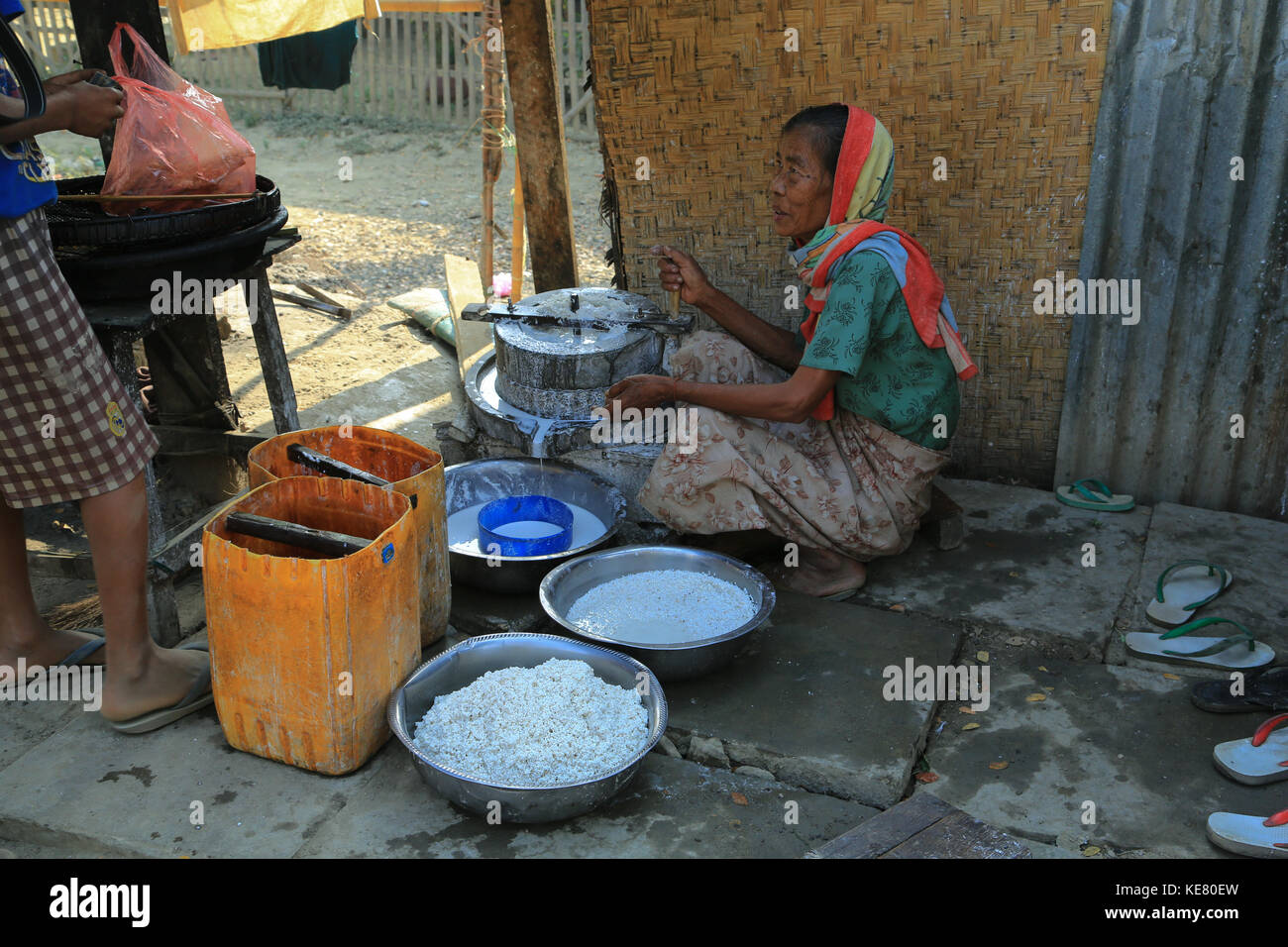 Nyaunghtaw Village is on the left (east) bank of the Irrawaddy River in Ayeyarwaddy province in Myanmar (Burma). Woman grinding rice with machine. Stock Photo