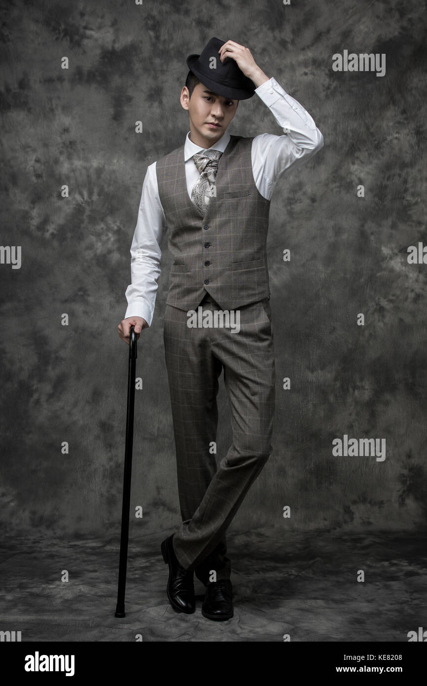 Young handsome man in retrostyle suit posing with a cane and hat Stock
