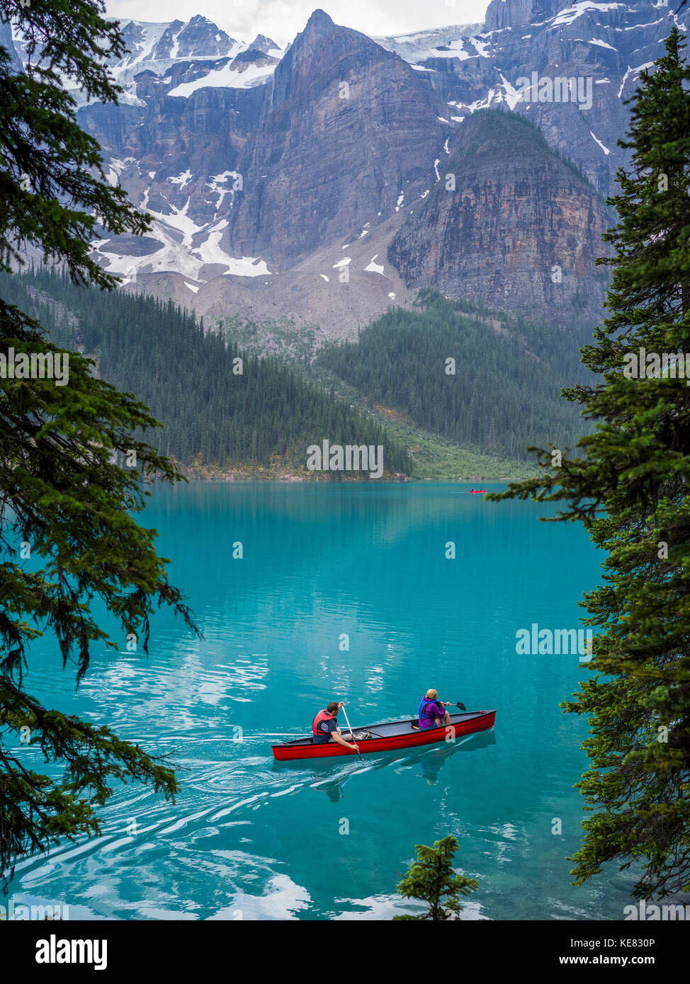 A red canoe in Moraine Lake with a cliff of the Canadian Rocky