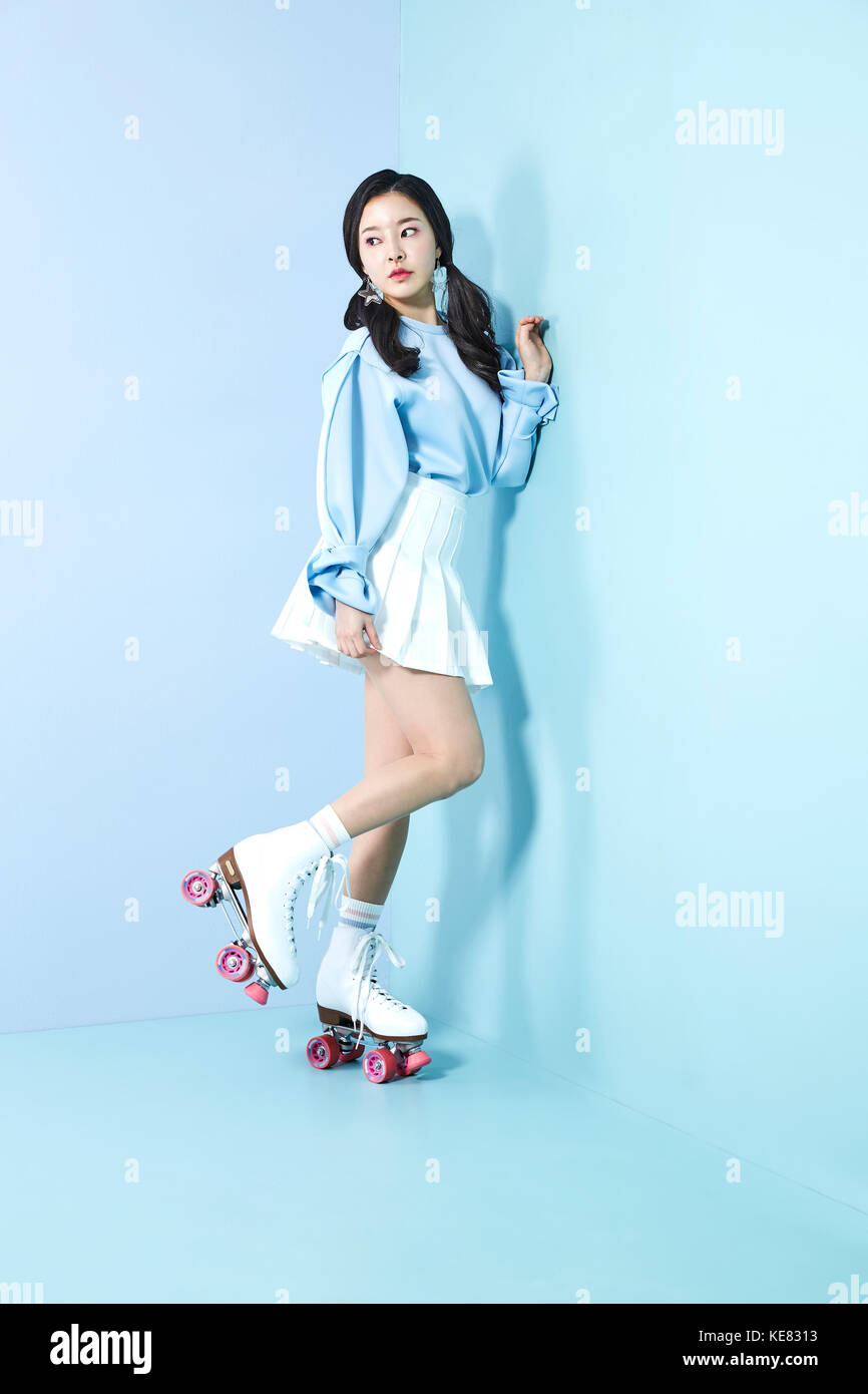 Young woman leaning against wall in roller skates on one foot looking aside Stock Photo