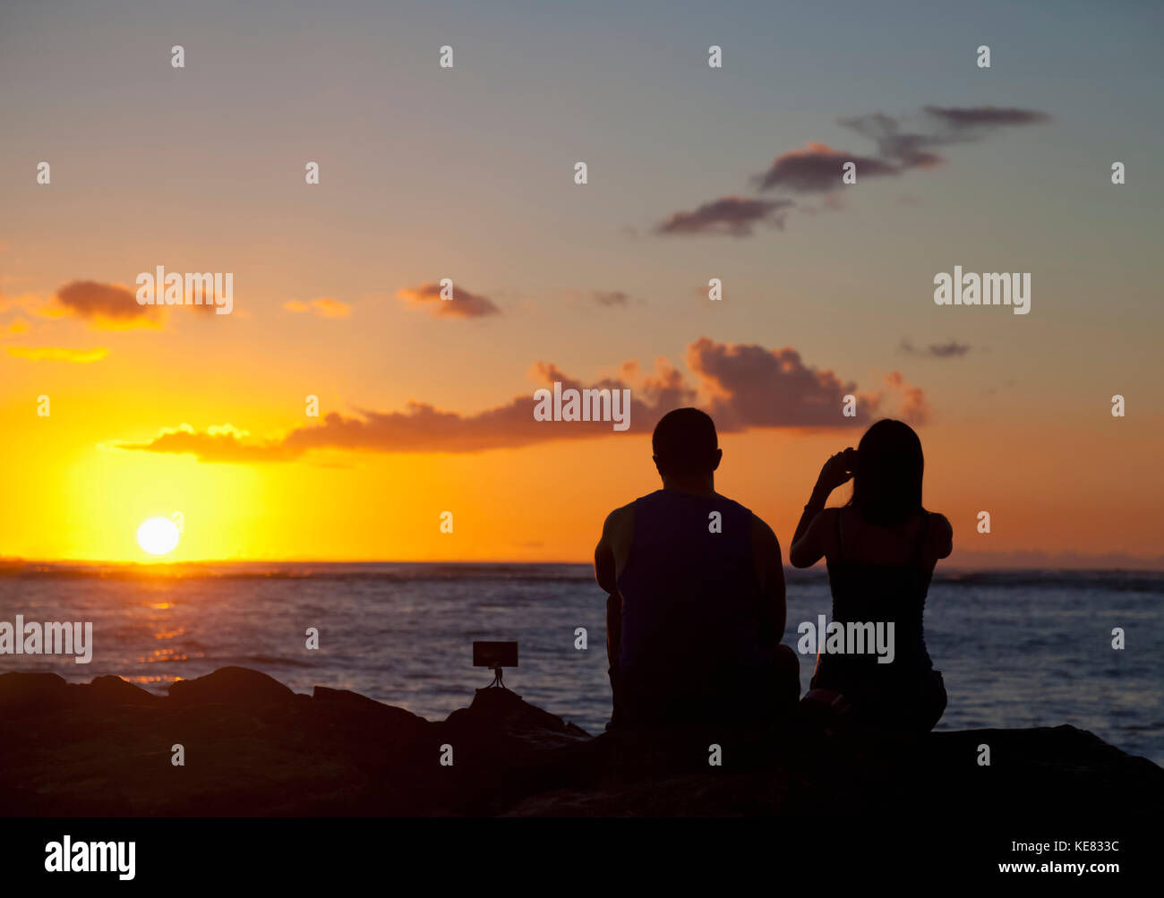 Silhouette of a couple taking pictures and watching the sunset on the beach, Waikiki; Honolulu, Oahu, Hawaii, United States of America Stock Photo