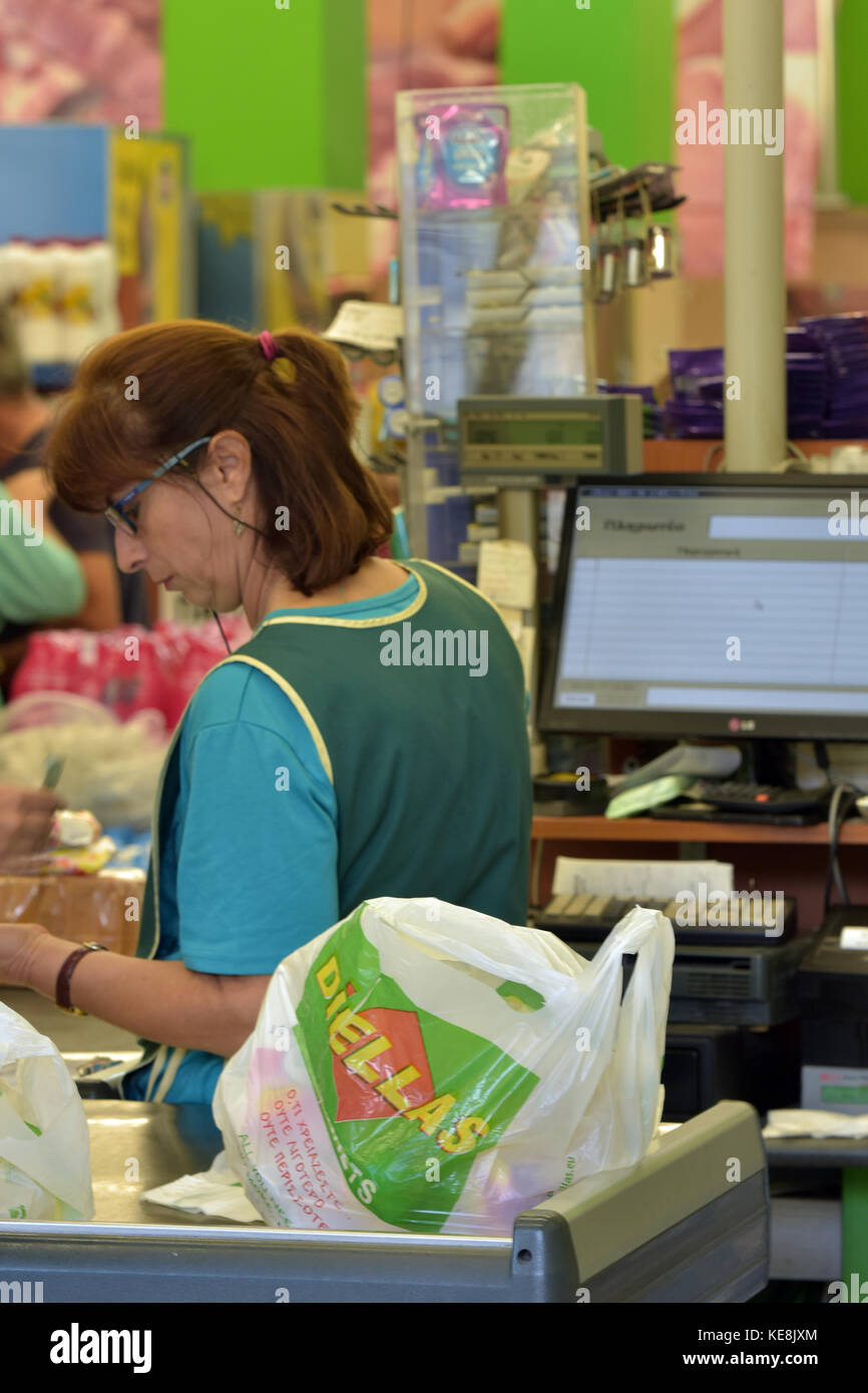 A lady or woman working on the checkouts at a big supermarket working the cash register and till taking money and cards from the customers buying food Stock Photo