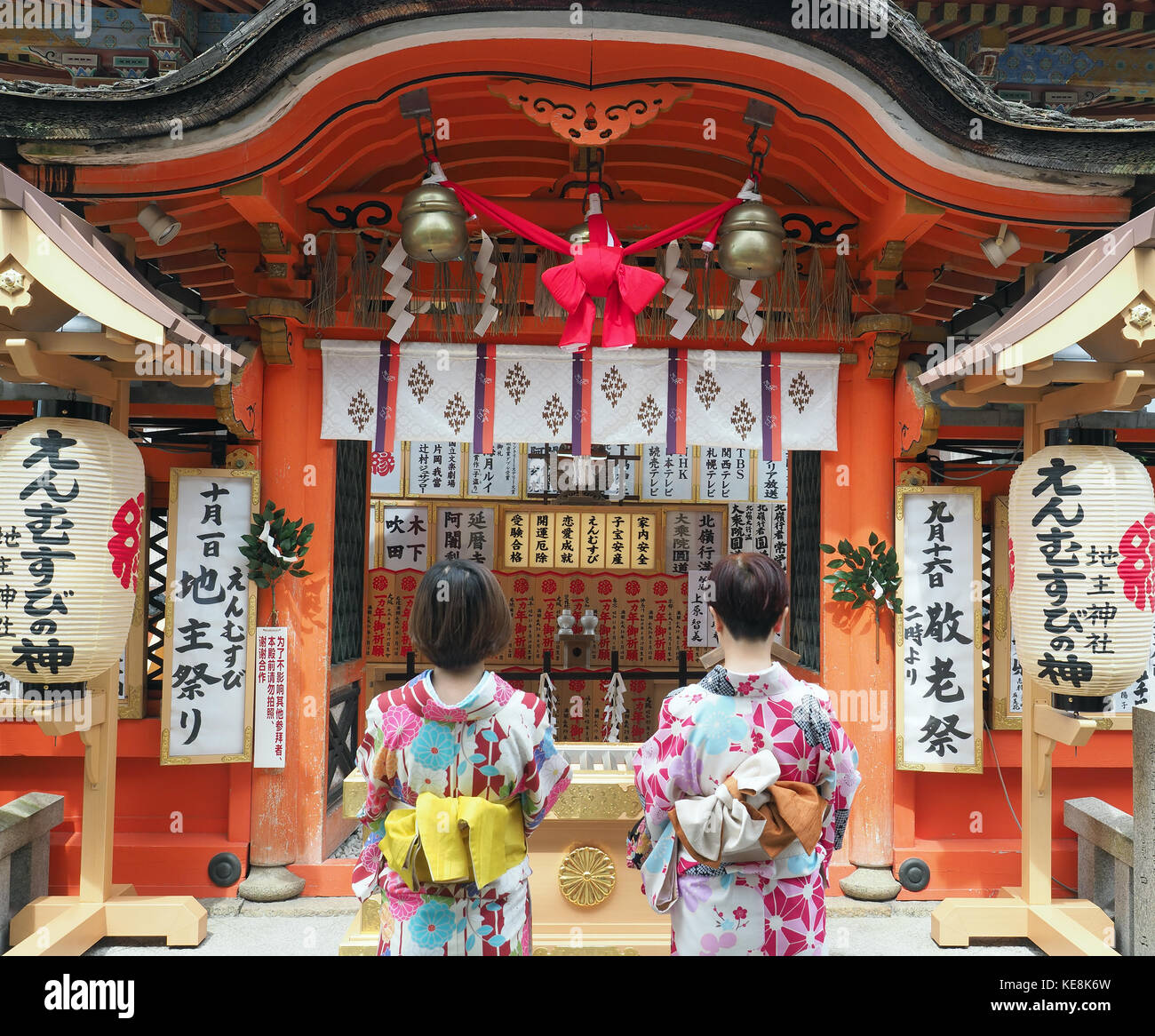 Rear view of two girls wearing kimonos making a wish at the Jishu-jinja inner shrine located within the Kiyomizu-dera temple in Kyoto Japan Stock Photo