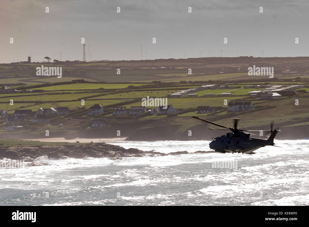 Helicopter in silhouette heads across surf towards a beach and landfall Stock Photo