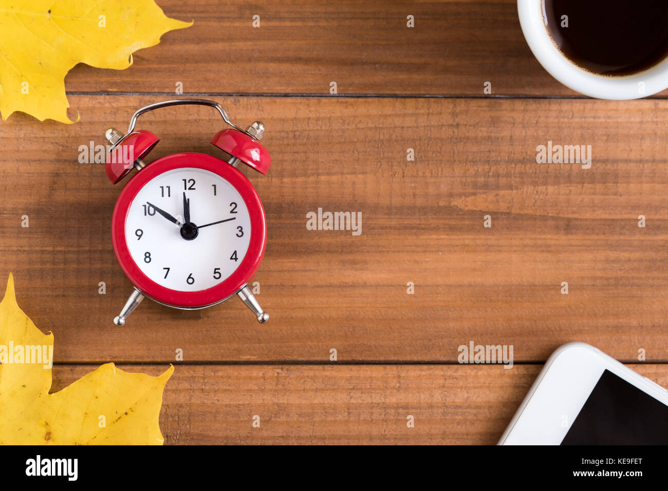 Top view of alarm clock, cup of coffee, smartphone and autumn maple