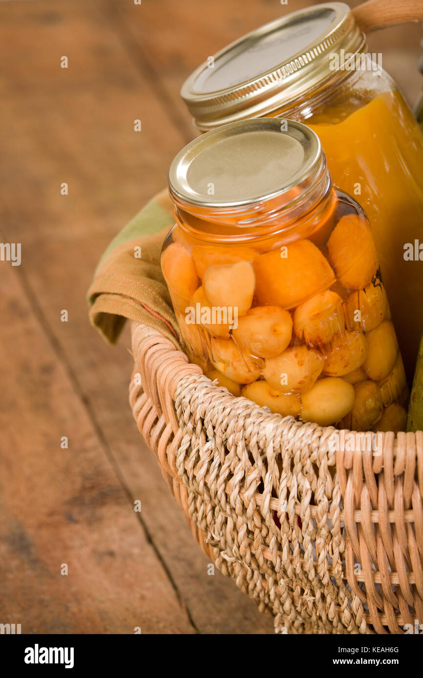 Home-canned produce (Rainier cherries and butternut squash soup) in a large wicker basket resting on a rustic wood tabletop Stock Photo