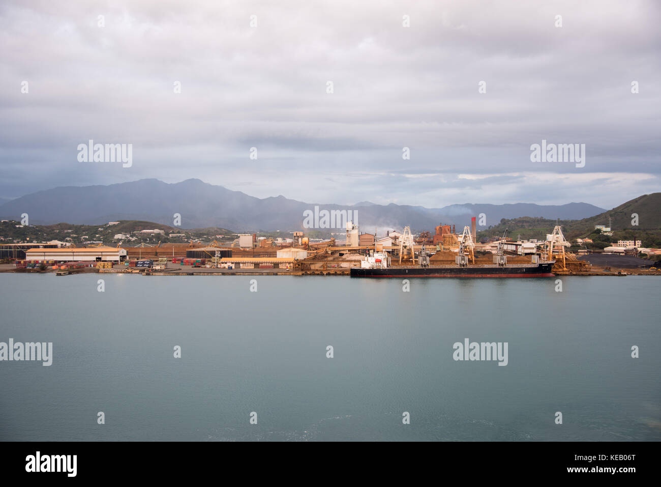 NOUMEA, NEW CALEDONIA-NOVEMBER 25,2016: Bulk carrier at commercial dock with SLN Plant, smoke stack, and mountain view in Noumea, New Caledonia. Stock Photo