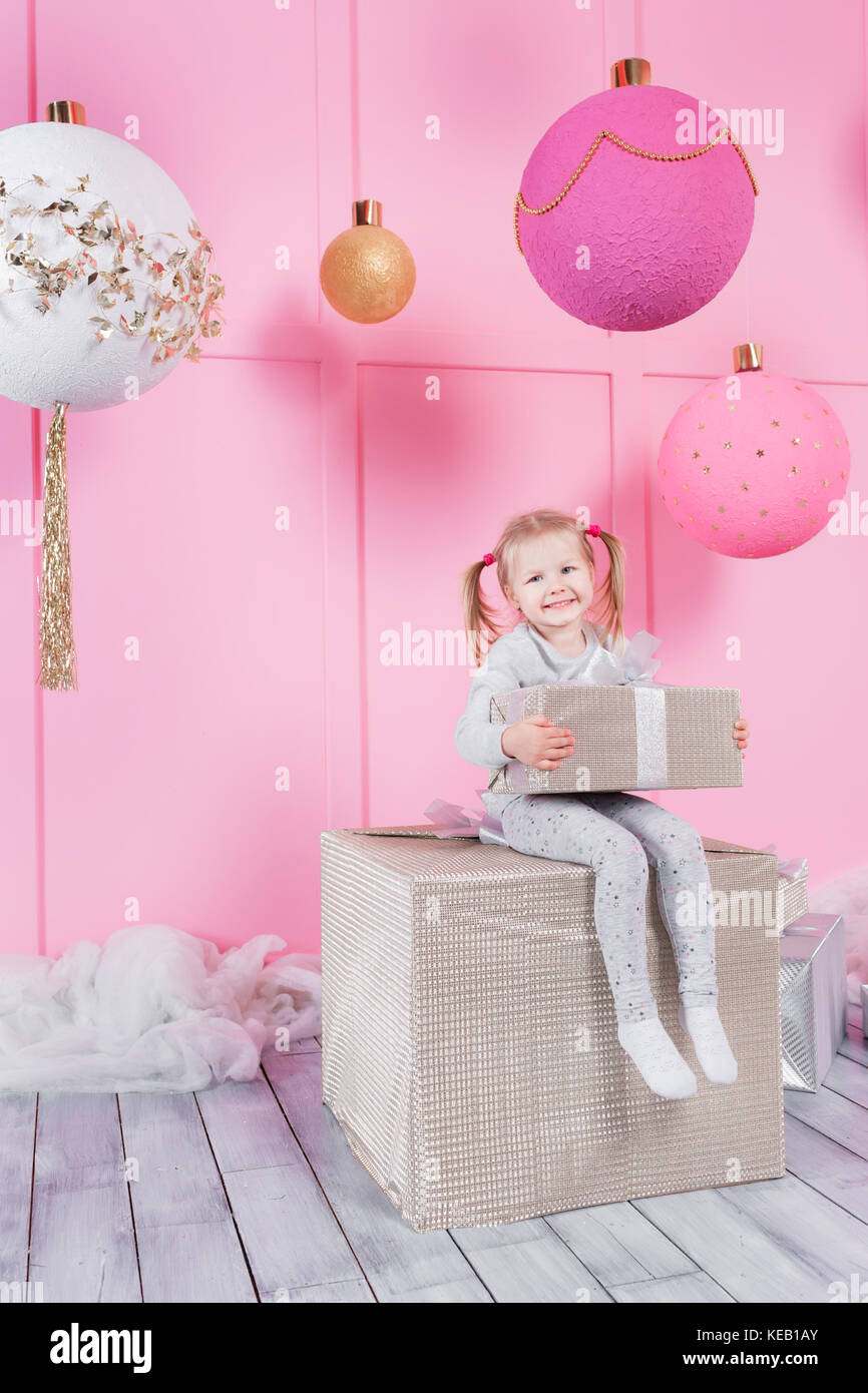 cute little girl sitting in a chair and opens a box with a present for ...