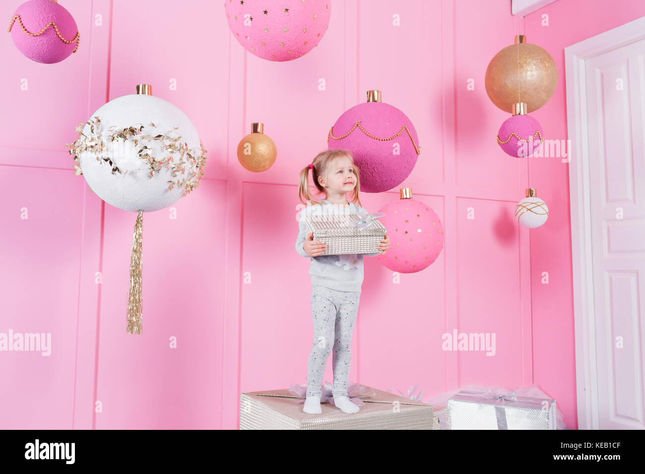 cute little girl sitting in a chair and opens a box with a present for ...