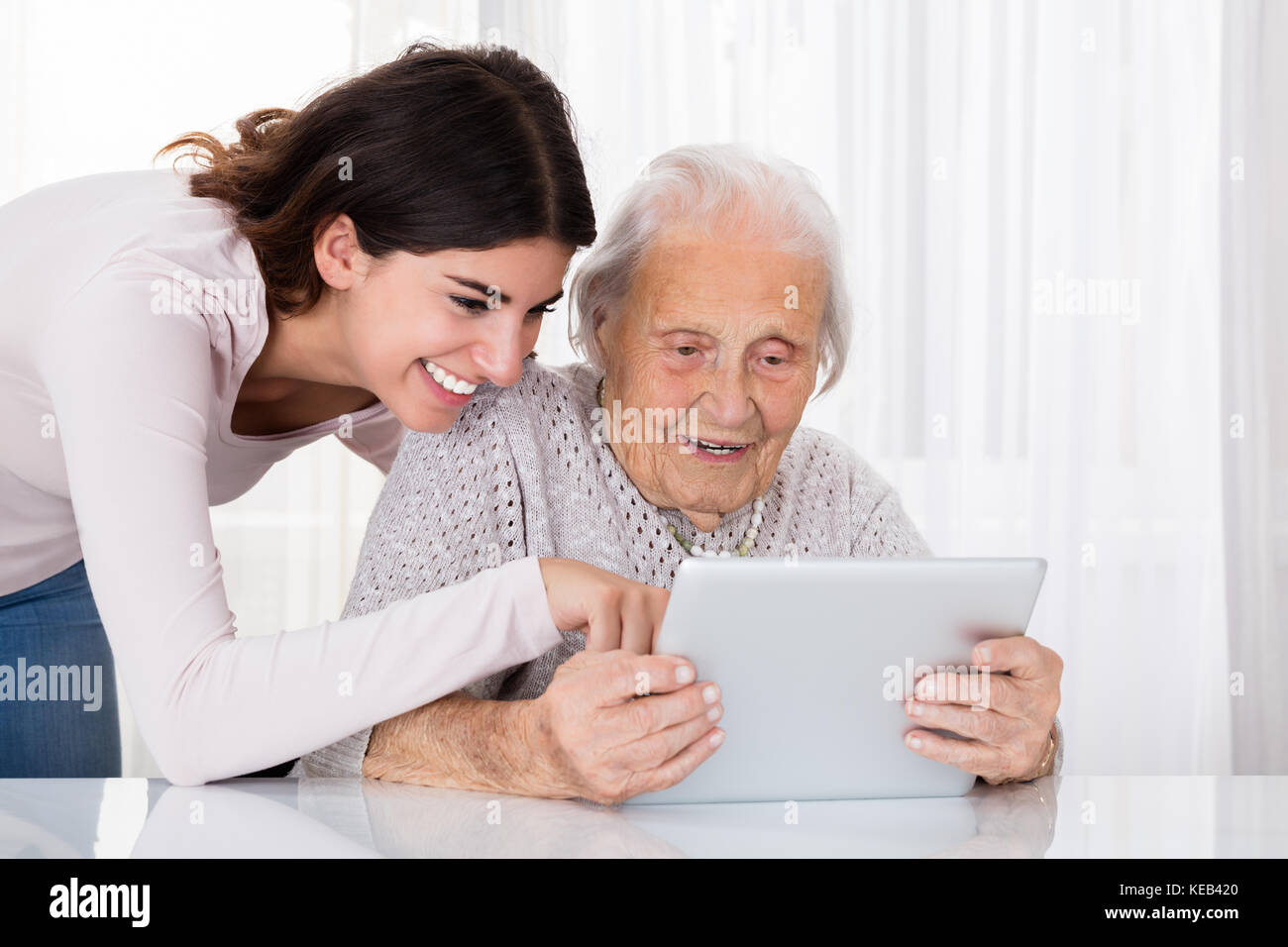 Young Woman Helping Her Grandmother For Using A Laptop On Desk At Home Stock Photo