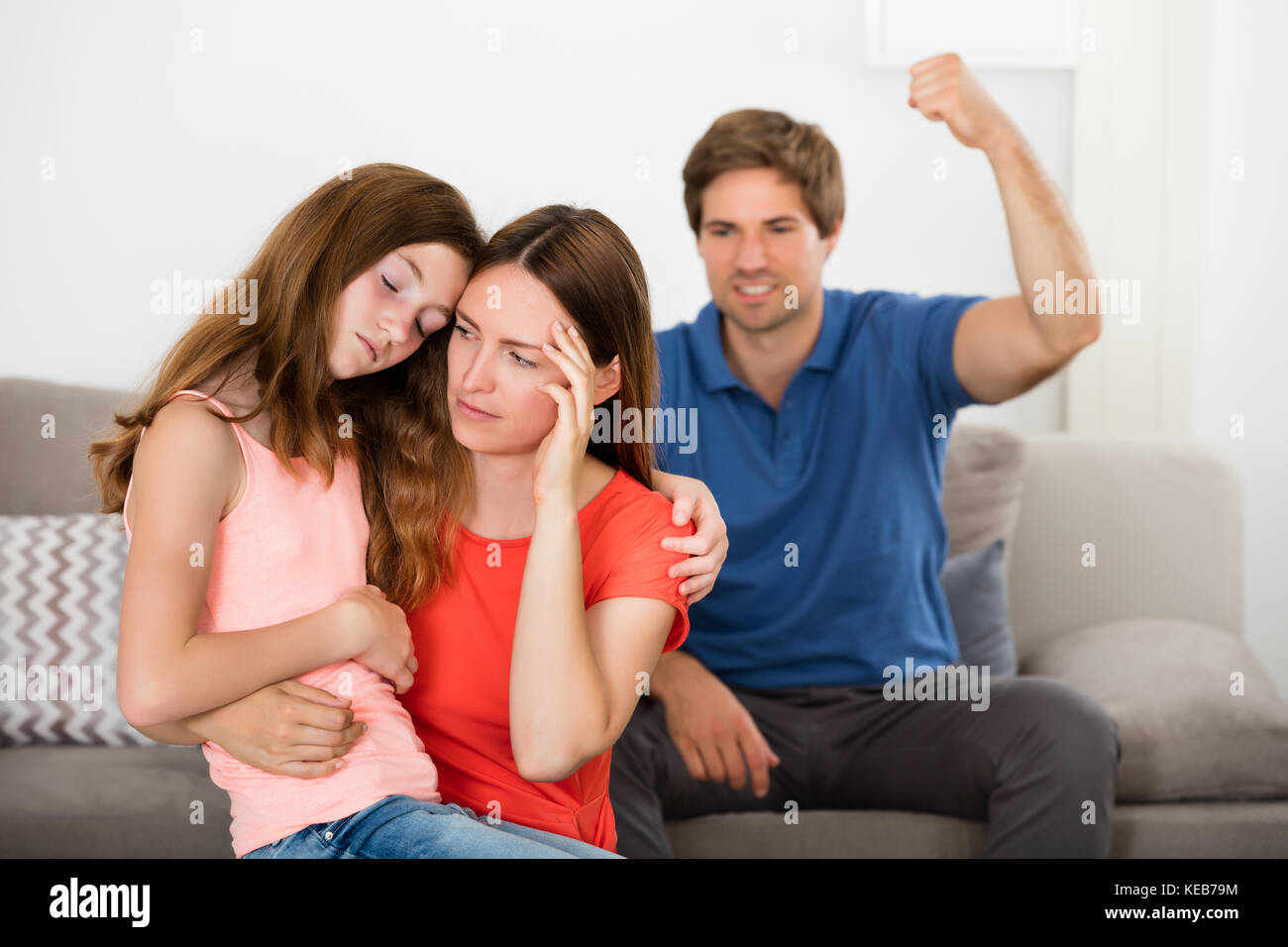 Depressed Mother And Daughter In Front Of Violent Father Sitting On Sofa Stock Photo