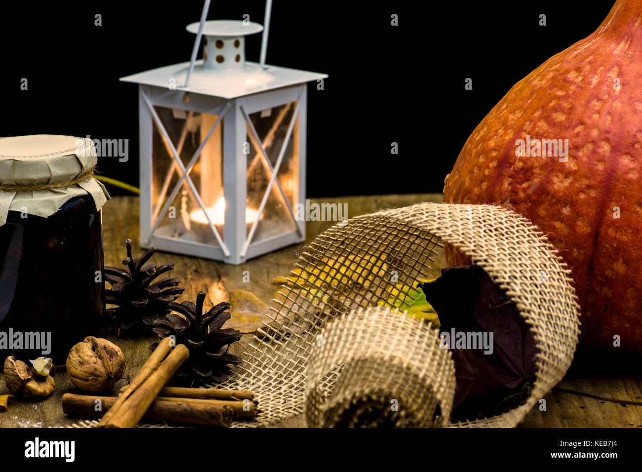 Dark autumn still life with pumpkin, candle and lamp, with yellow leaves of trees on old wooden table board - atmosphere with warm colors Stock Photo