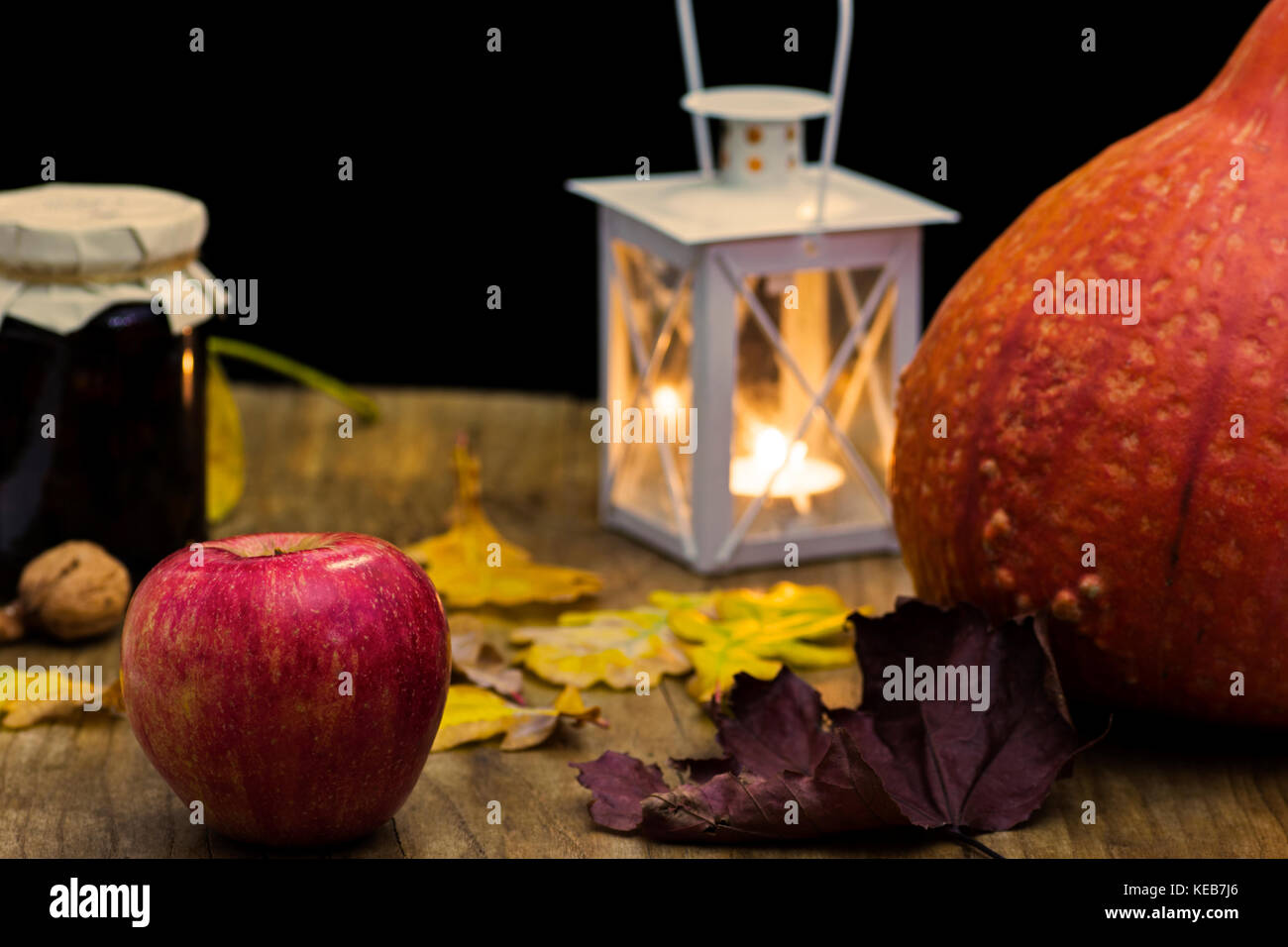 Dark autumn still life with pumpkin, candle and lamp, with yellow leaves of trees on old wooden table board - atmosphere with warm colors Stock Photo