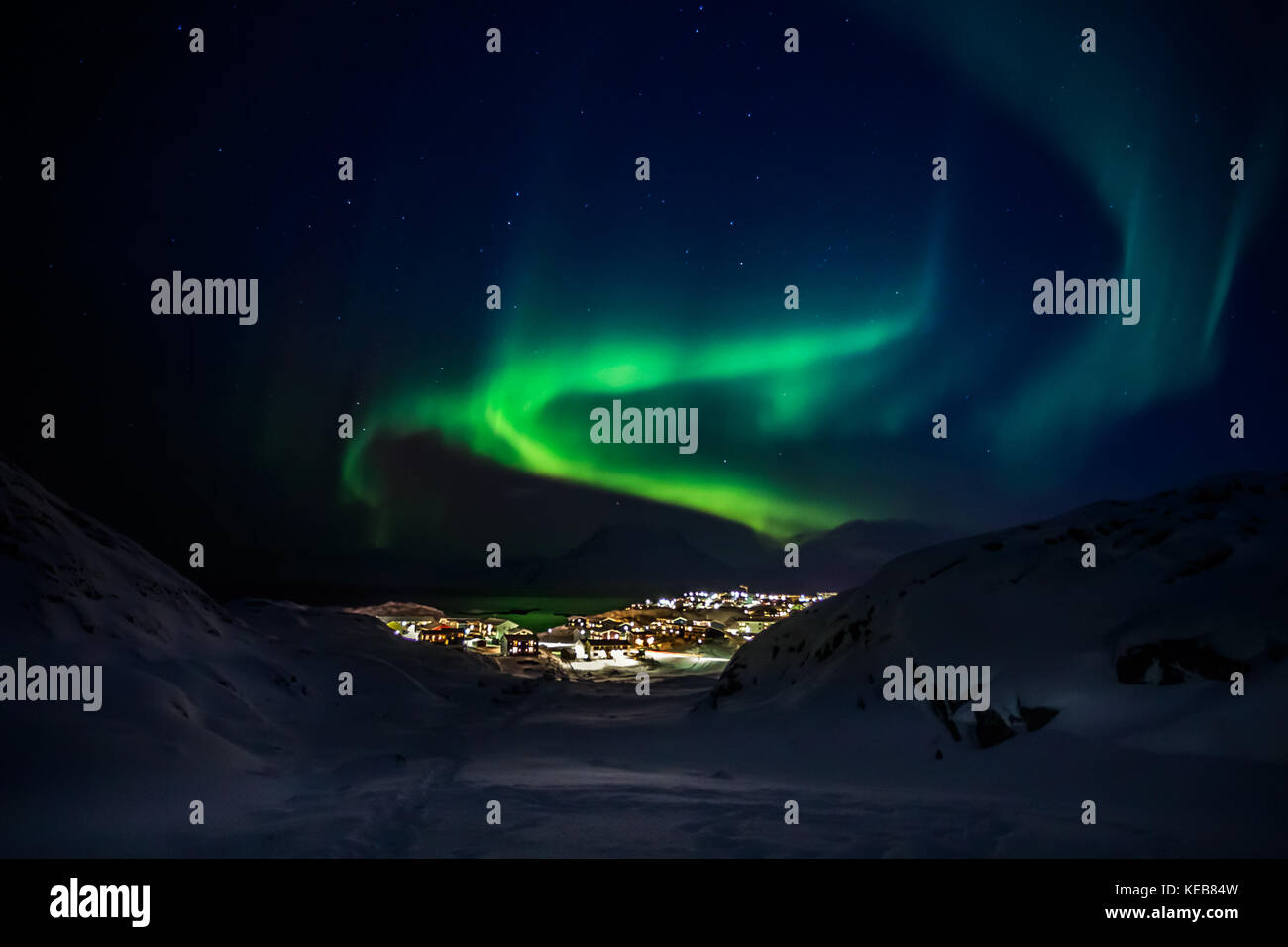 Green lights of Aurora Borealis with shining stars over the mountains and highlighted city, Nuuk, Greenland Stock Photo