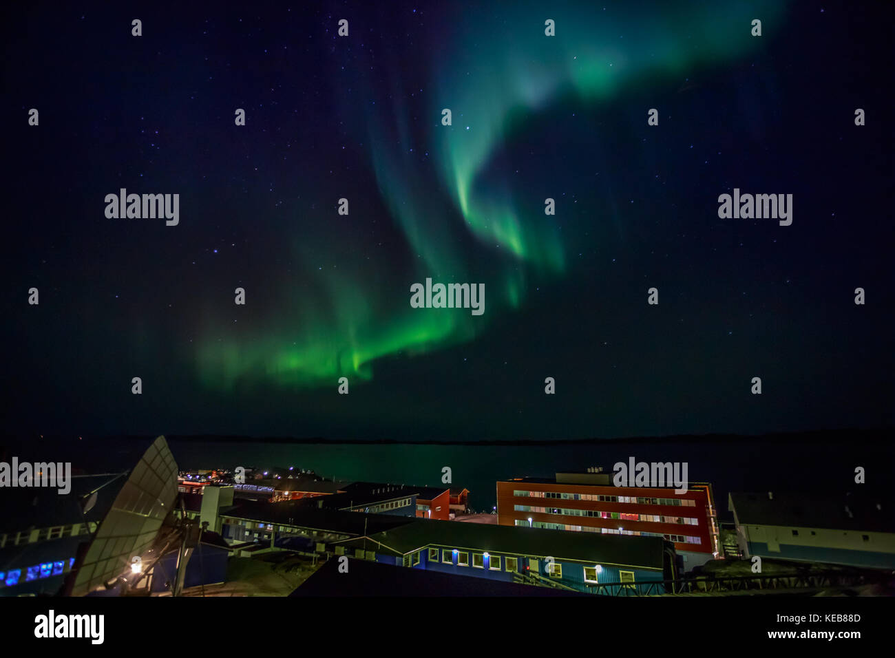 Green lights of Aurora Borealis with shining stars over the night bay and highlighted buildings of Nuuk city, Greenland Stock Photo