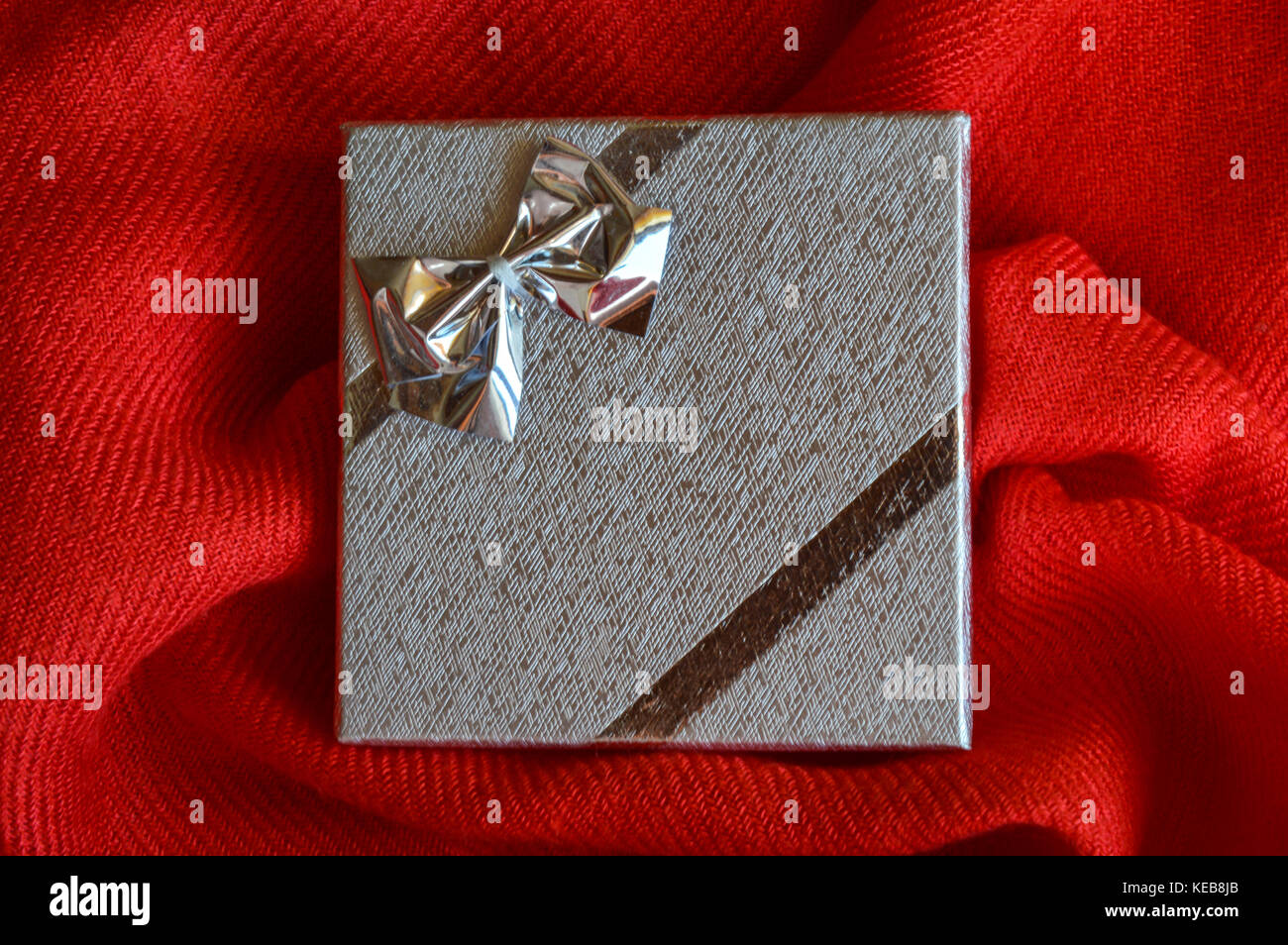 A silver gift box with a bow on red fabric background Stock Photo - Alamy