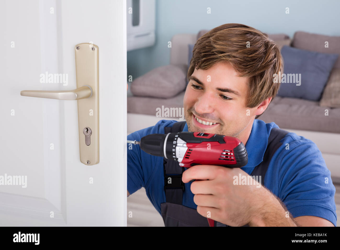 Smiling Young Carpenter Install Door Lock Using Wireless Screwdriver At
