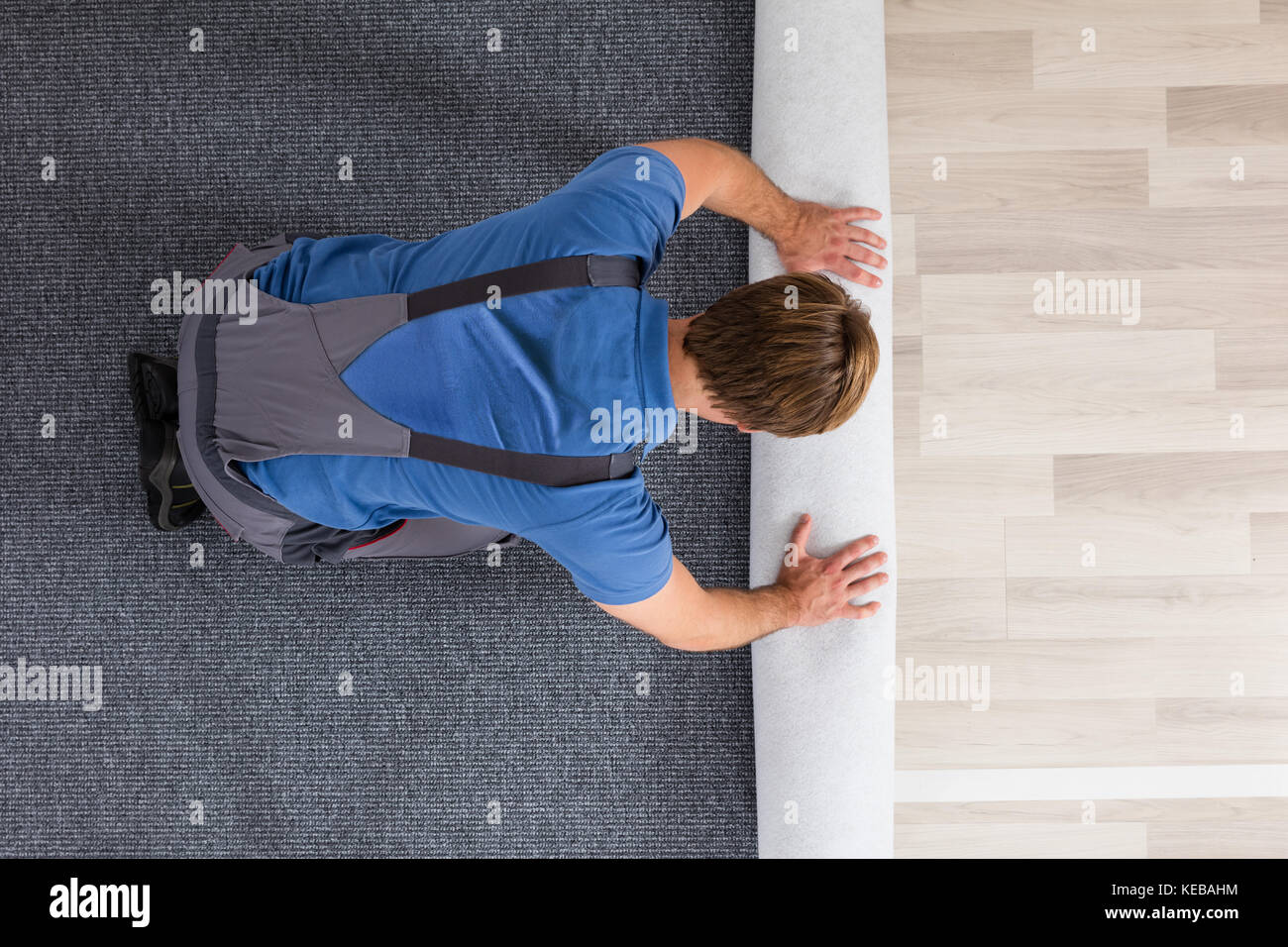 High Angle View Of Male Worker In Overalls Rolling Carpet On Floor At Home Stock Photo