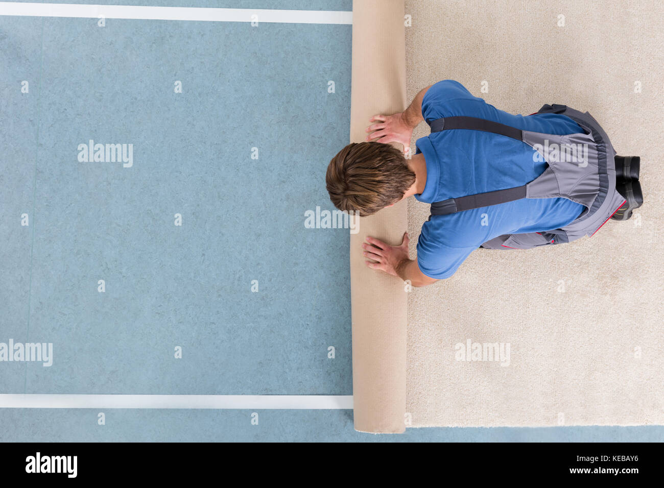 High Angle View Of Craftsman In Overalls Unrolling Carpet On Floor Stock Photo