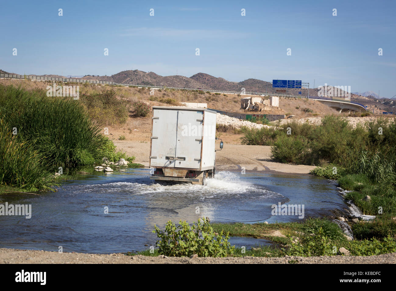 A river ford.  A ford is a shallow spot in a river or stream which permits traffic to drive across, or people to wade across.  This vehicle is crossin Stock Photo