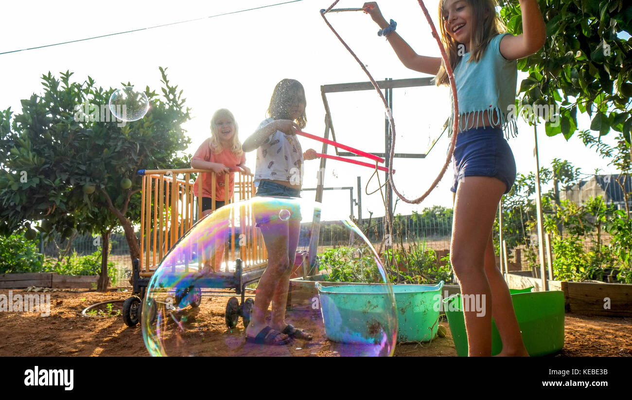 Young girl makes a large soap bubble while other excited children watch and wait their turn Stock Photo