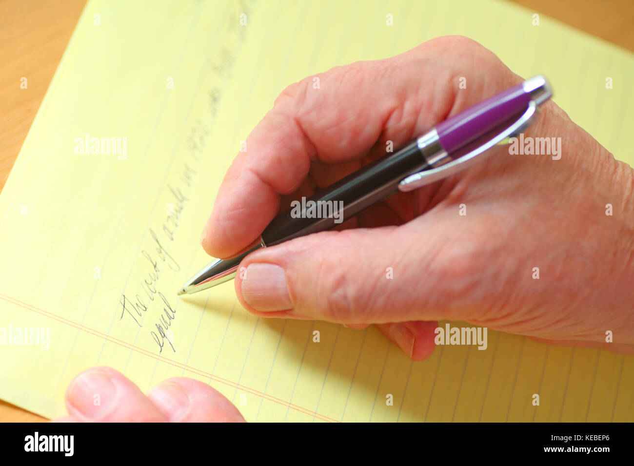 Older man writes in cursive on a ruled yellow pad of paper Stock Photo