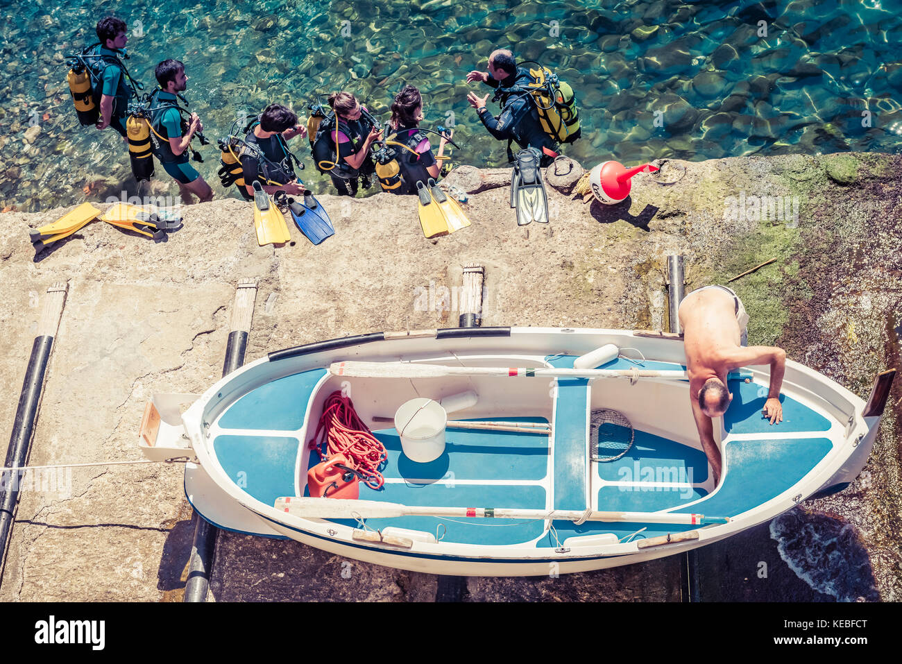 A boat is hauled out of the sea as a group of scuba divers enters the sea Stock Photo