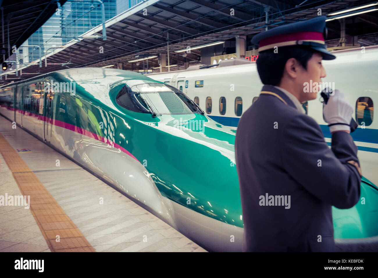 On Japan Railways both the trains and the service are polished. A shinkansen leaves Tokyo Station with a guard in the foreground. Stock Photo