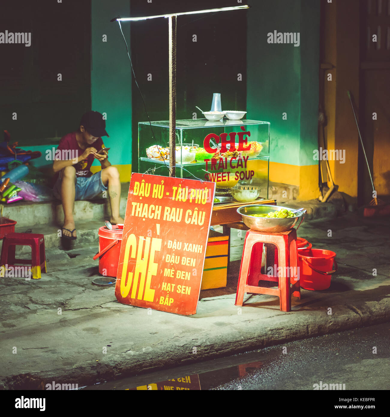 A quiet night in Hoi An as a streetfood vendor plays on his mobile phone Stock Photo