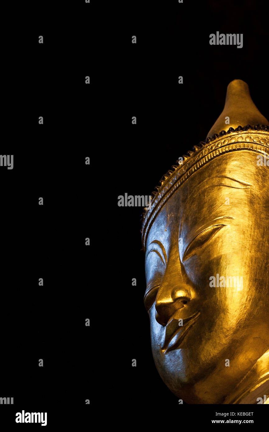 Big Buddha head with eyes closed in contemplation. A Golden Buddha statue isolated on black background in a cave temple in Thailand. Sacred holy place Stock Photo
