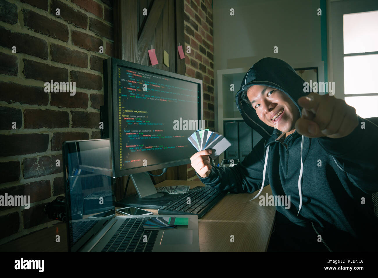 professional young male hacker criminal showing many personal credit card and pointing camera. Stock Photo